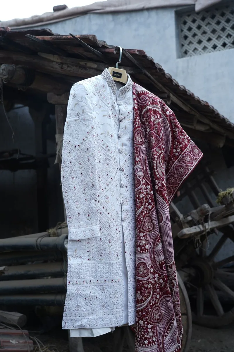 A groom wearing an embroidered cream sherwani with a red dupatta