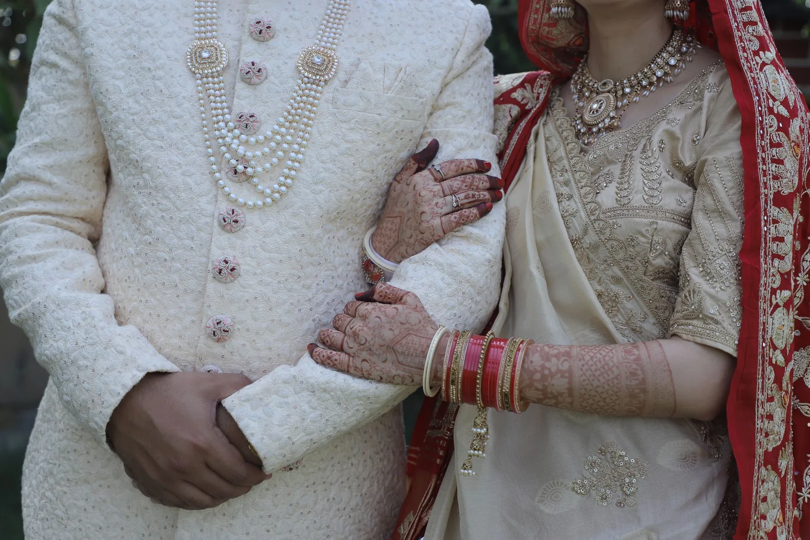 A couple dressed in fine Indian wedding attire, the groom in a cream sherwani and the bride in gold and red